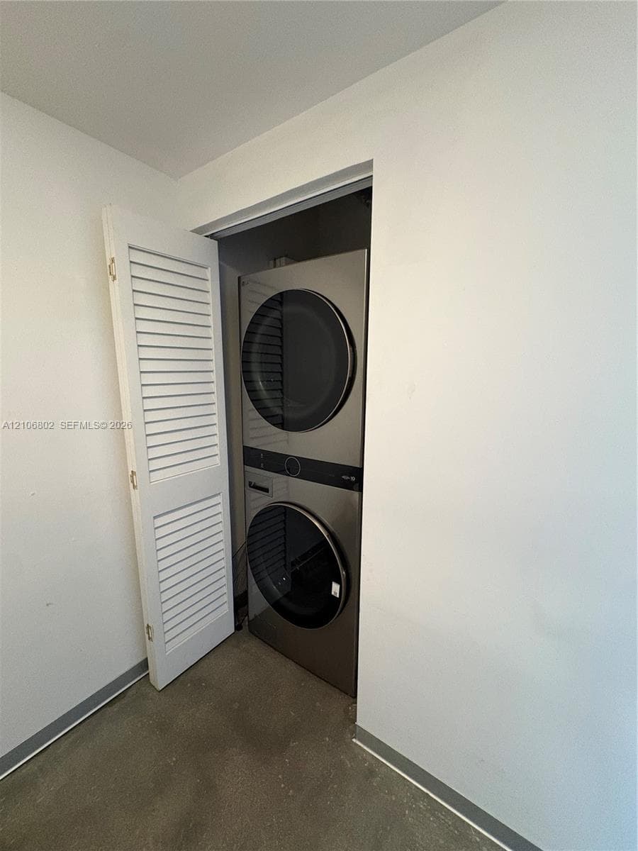 Stacked stainless steel laundry center enclosed by a white louvered door