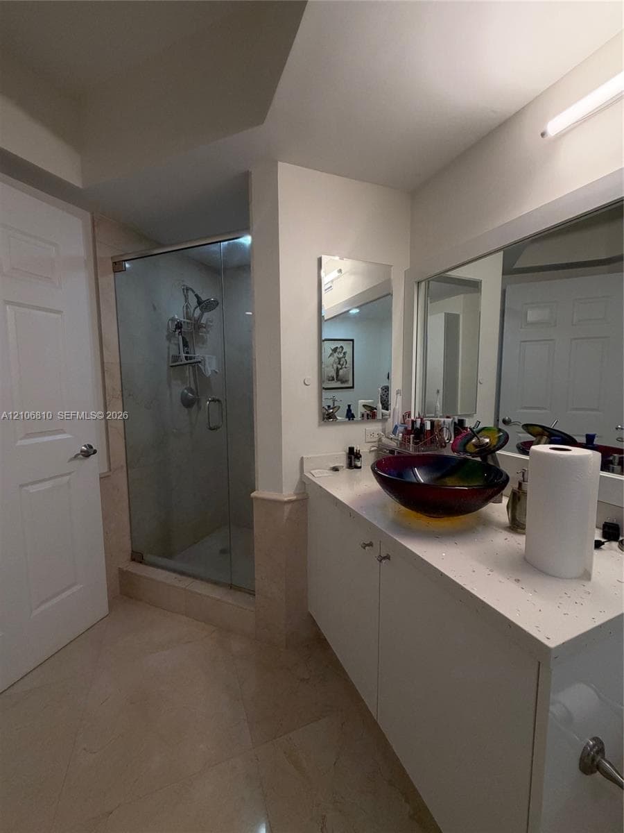 Bathroom featuring a solid-surface vanity countertop, vessel sink, walk-in shower with a glass enclosure, large wall-mounted mirror, and stone-tile flooring