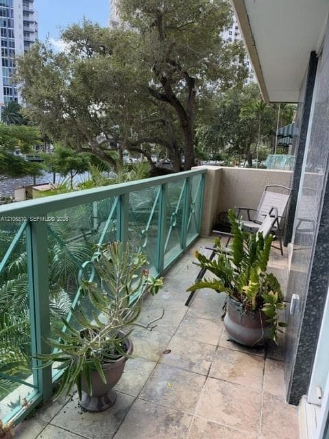 Covered balcony featuring stone-finish tile flooring, decorative metal railing, and high-rise exterior cladding