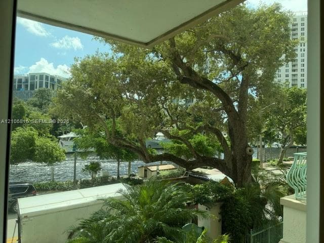 Exterior balcony featuring decorative metal railings, concrete columns, and natural scenery including mature trees, greenery, and water frontage