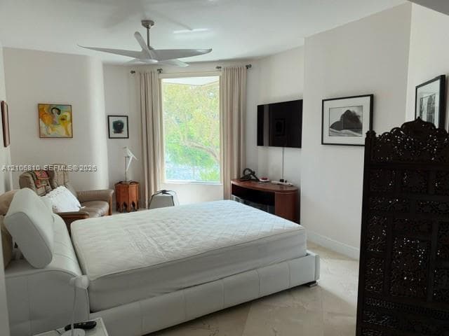 Spacious room featuring light-toned stone flooring, a ceiling fan, and a large bay window