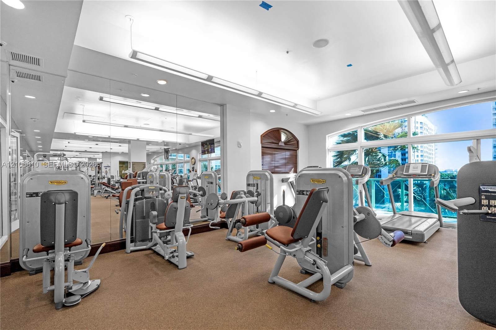 Fitness center featuring full-wall mirrors, recessed lighting, multi-station exercise equipment, rubberized flooring, and large windows with exterior access