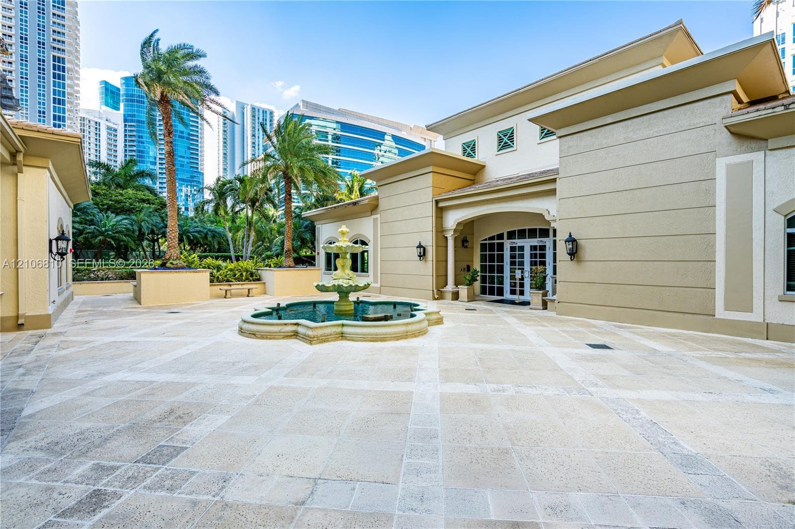 Courtyard featuring a tiered stone fountain, stone paver flooring, exterior wall-mounted lanterns, and mature palm trees