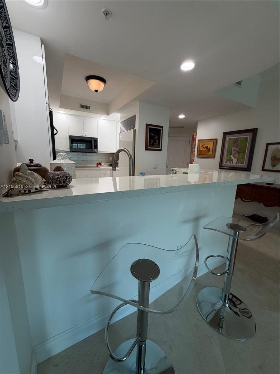 Kitchen featuring white cabinetry, solid-surface countertop, tile backsplash, built-in microwave, and recessed lighting