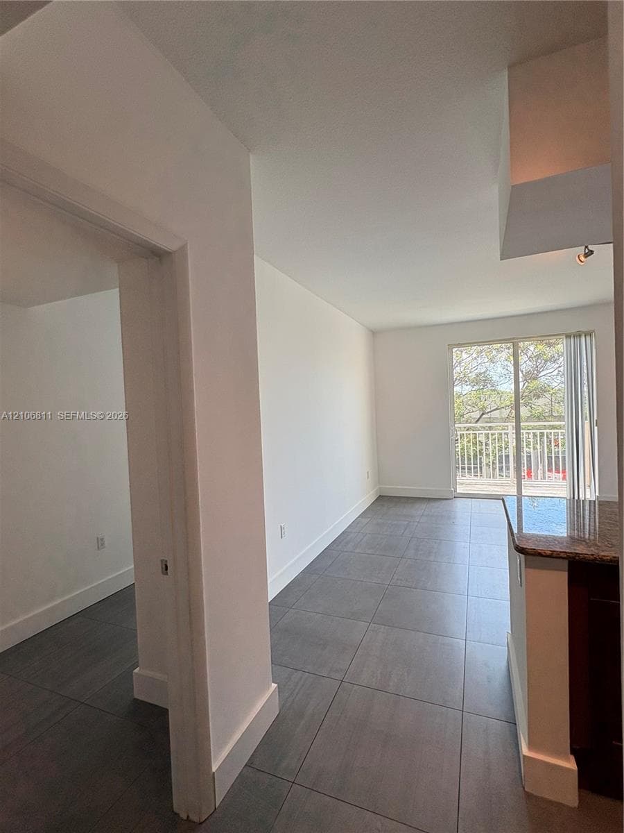 Open-concept interior featuring large-format ceramic tile flooring, stone-surfaced peninsula, and sliding glass door with access to a railed exterior balcony