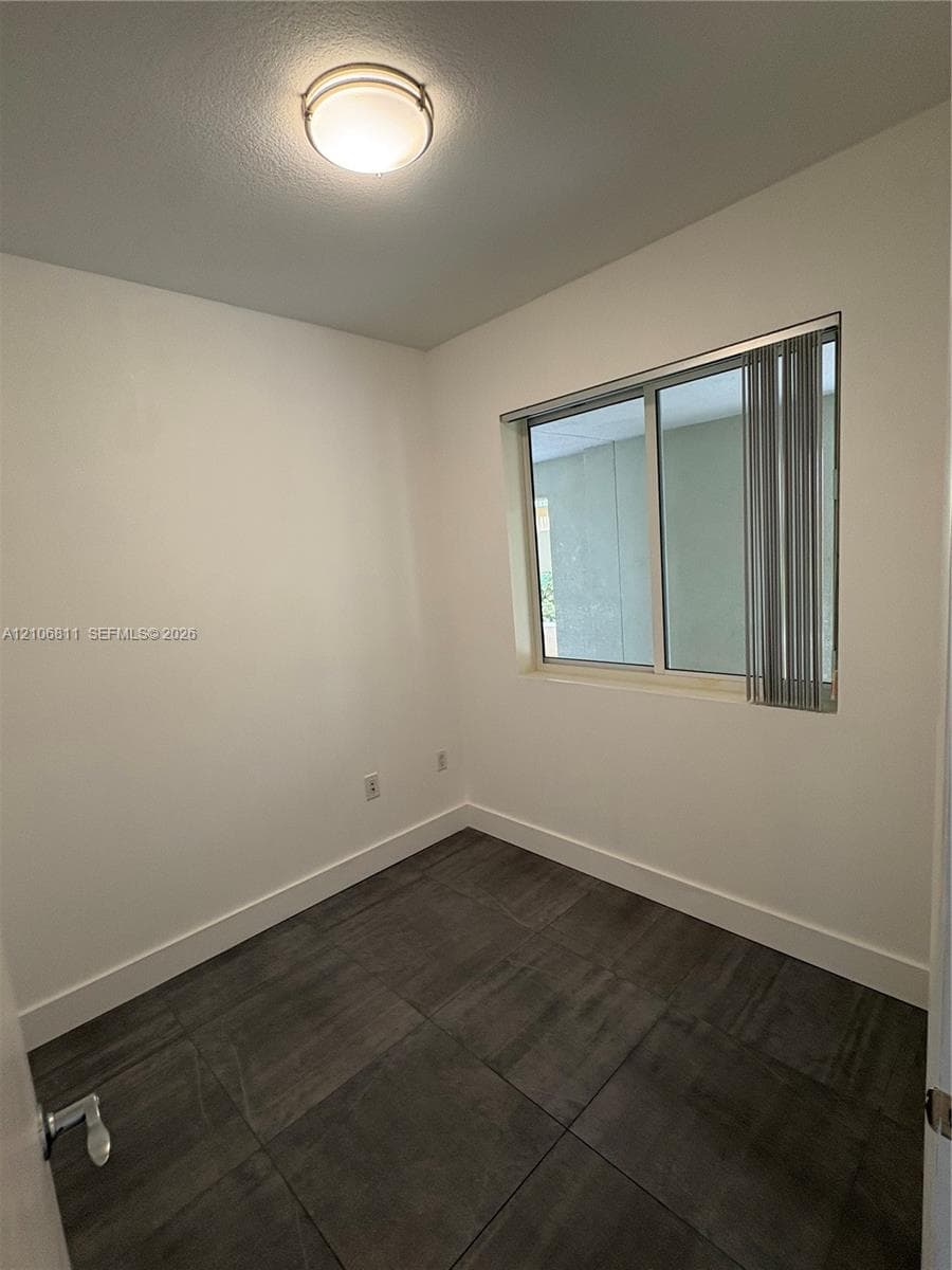 Room featuring large-format dark tile flooring, a dual-pane sliding window with vertical blinds, and a circular flush-mount ceiling light fixture