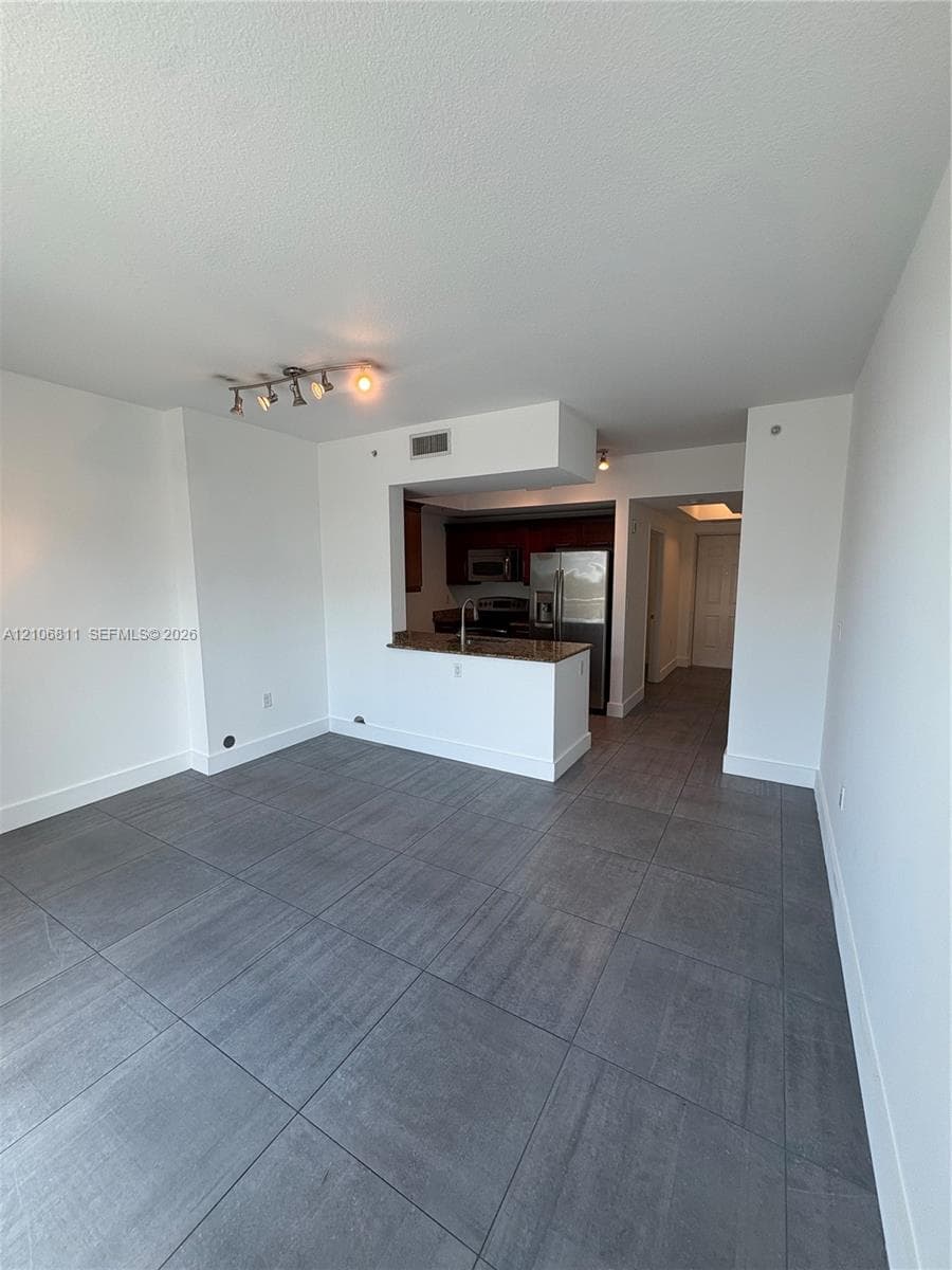 Open-concept interior featuring large-format tile flooring, a peninsula with stone countertops, stainless steel appliances, and track lighting