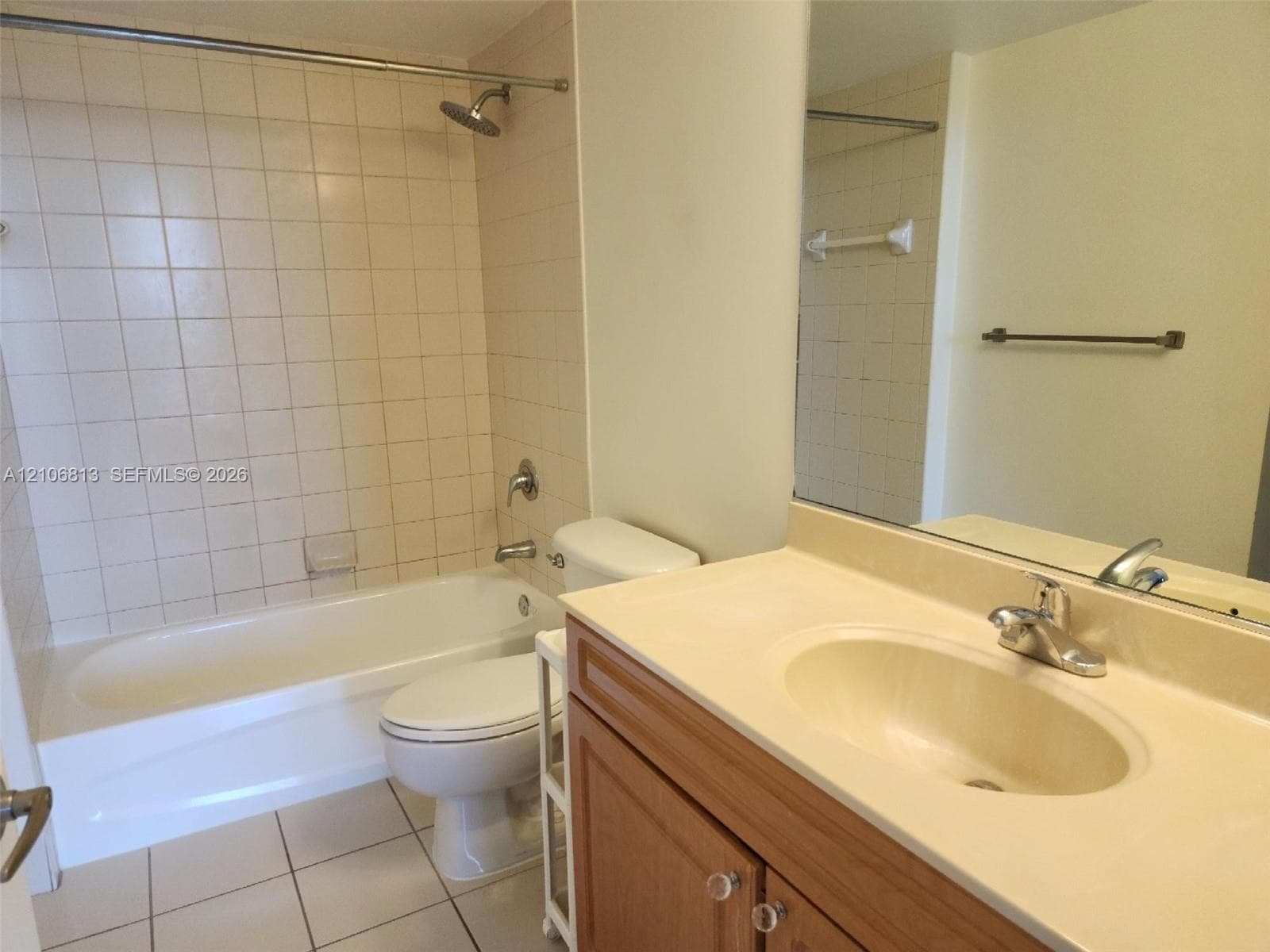 Bathroom featuring a tub-shower combination with ceramic tile surround, integrated vanity with a molded countertop sink, wood-finish cabinetry, and a full-width wall mirror