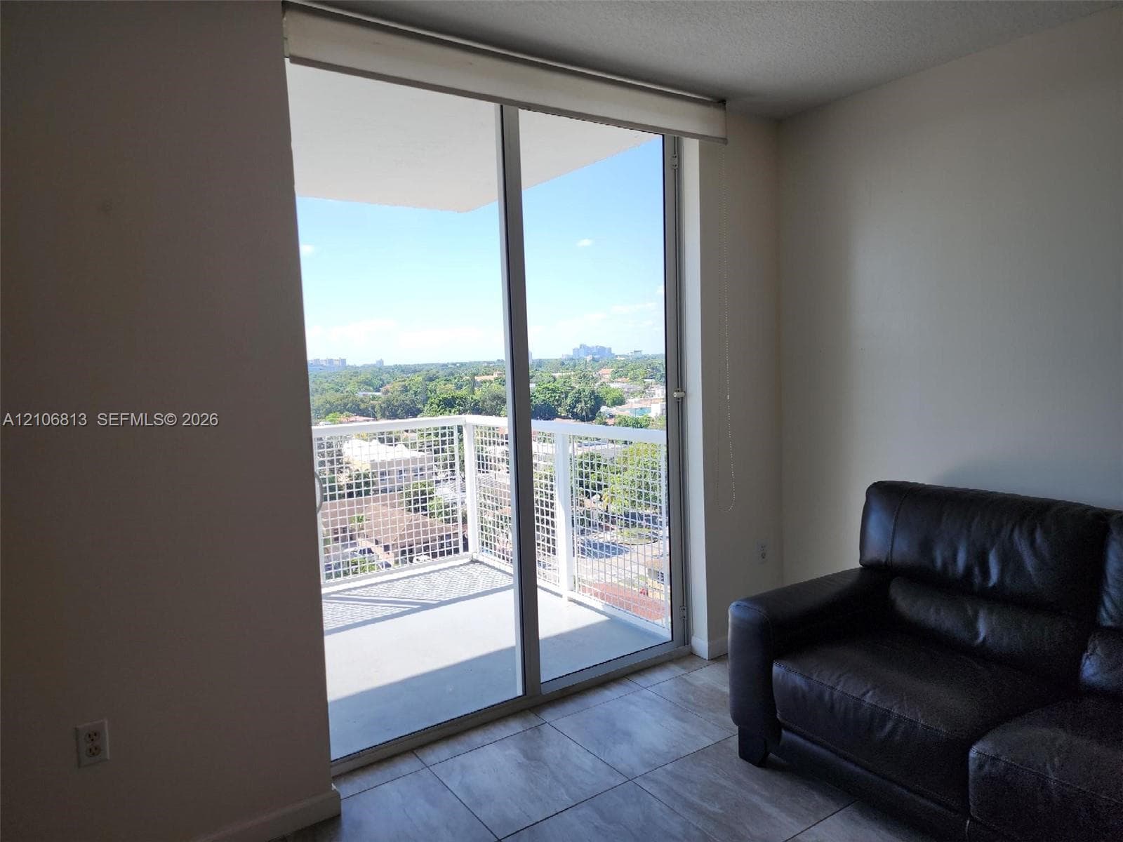 Floor-to-ceiling sliding glass door, private balcony with metal railing, and neutral tile flooring