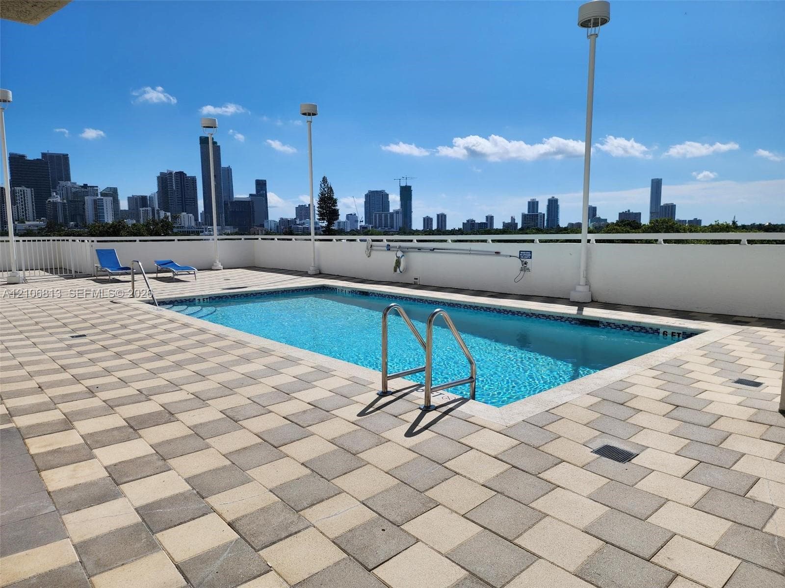 Rooftop swimming pool featuring a tiled deck, perimeter safety railing, built-in pool ladder, and urban skyline backdrop