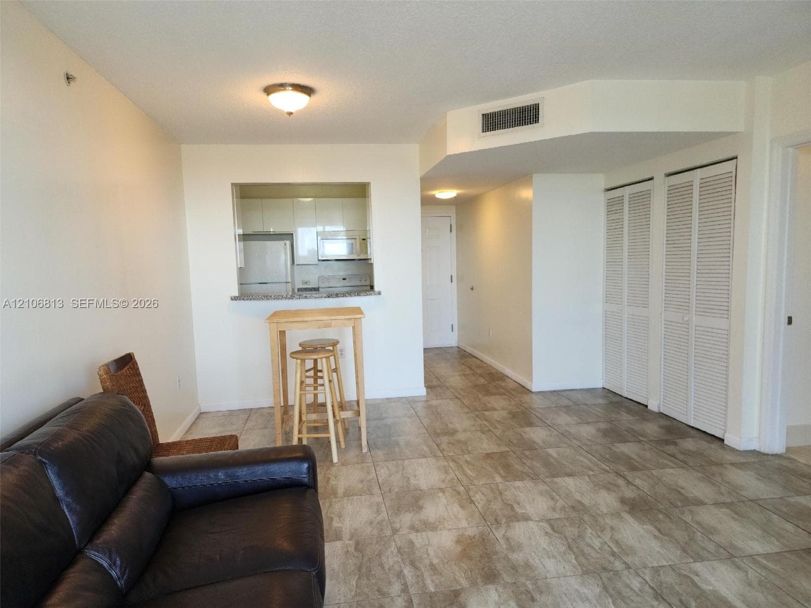 Open-concept interior featuring large-format stone-finish tile flooring, kitchen pass-through with stone countertop, and dual sets of louvered bifold closet doors