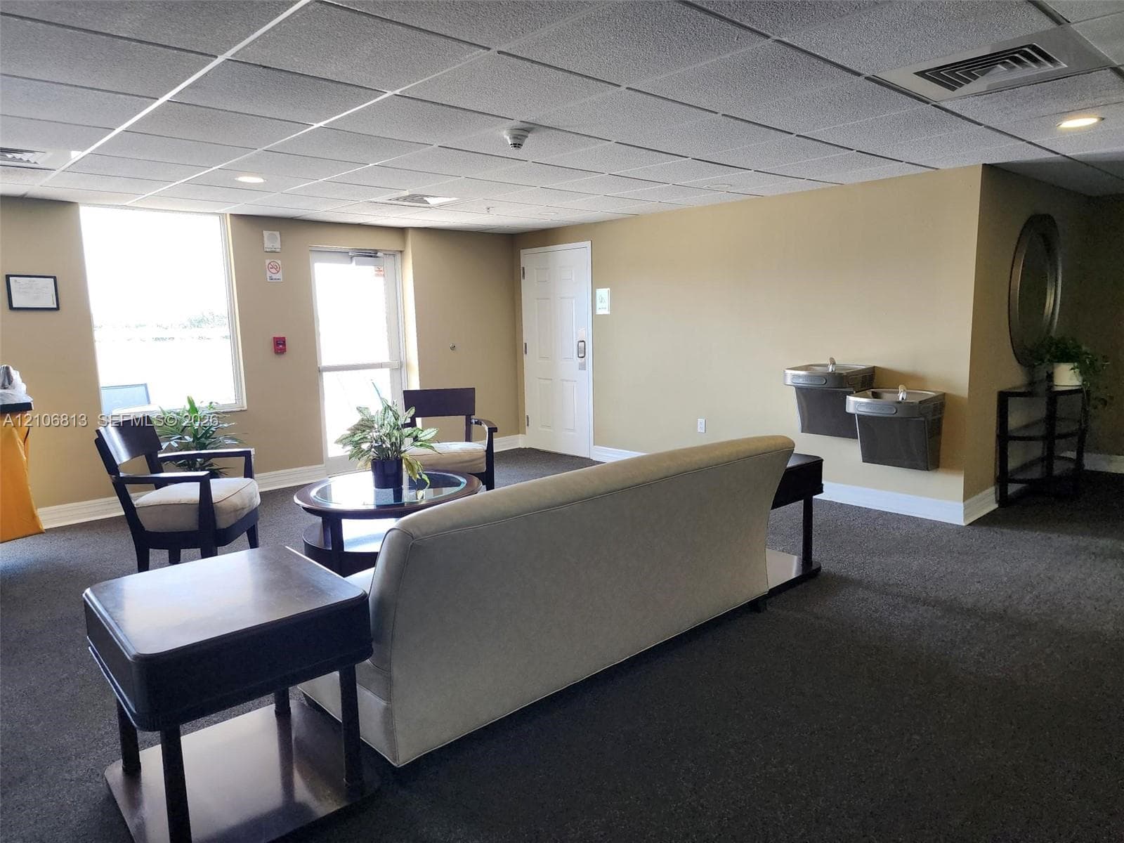Common area featuring a drop ceiling with recessed lighting, wall-to-wall carpeting, dual wall-mounted water fountains, and a glass-paneled exterior door