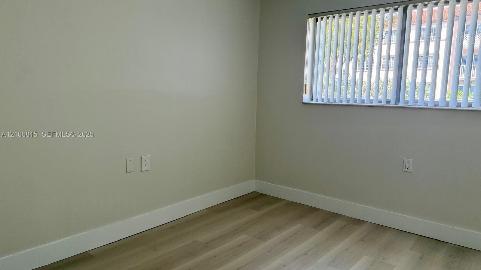 Room featuring light-toned wood-finish flooring, neutral wall paint, and window equipped with vertical blinds