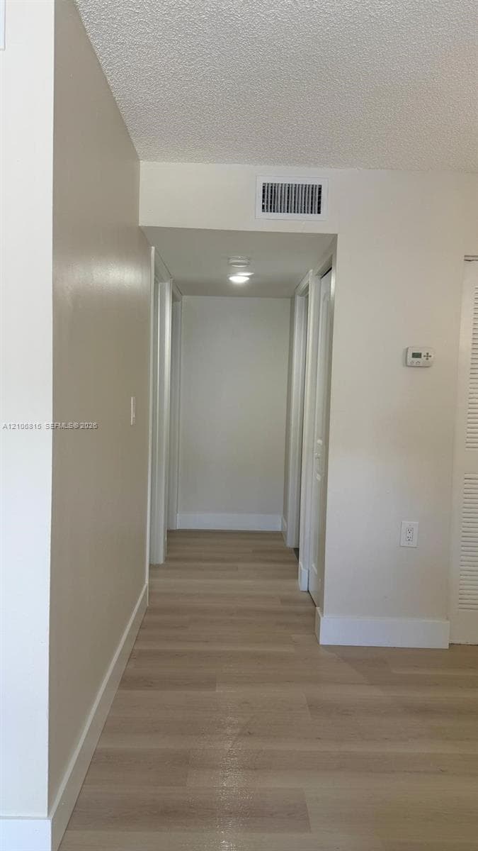 Interior hallway featuring wood-finish flooring, neutral wall paint, and ceiling-mounted light fixture