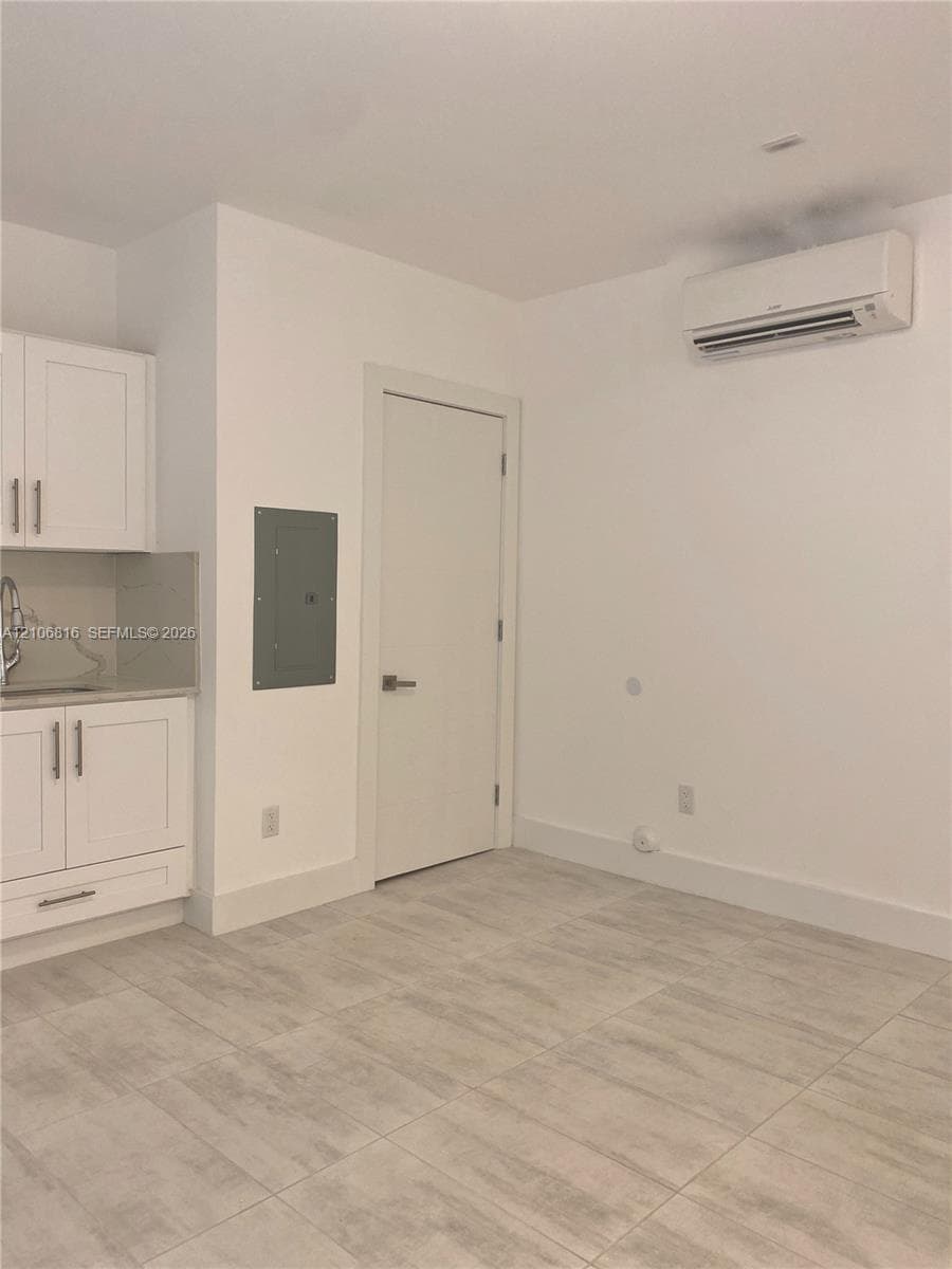 Kitchenette featuring white Shaker-style cabinetry, neutral stone-finish countertops, tile flooring, and wall-mounted air conditioning unit