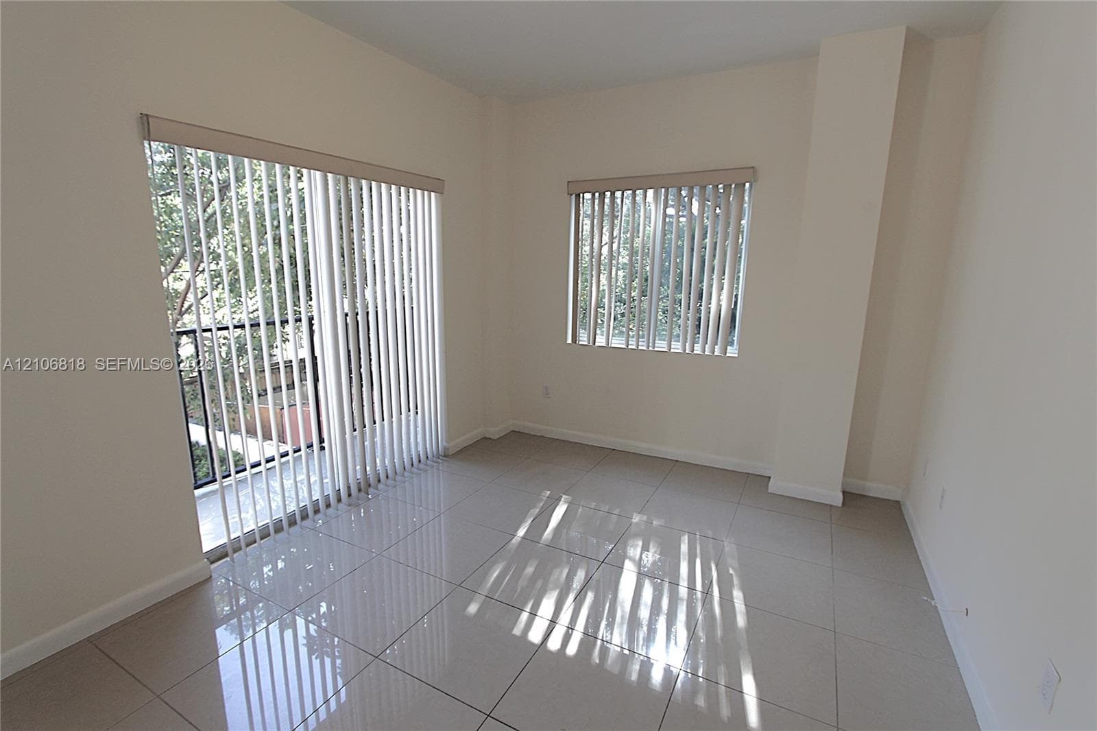 Neutral-toned tile flooring, large sliding glass door, vertical window blinds, and recessed wall design