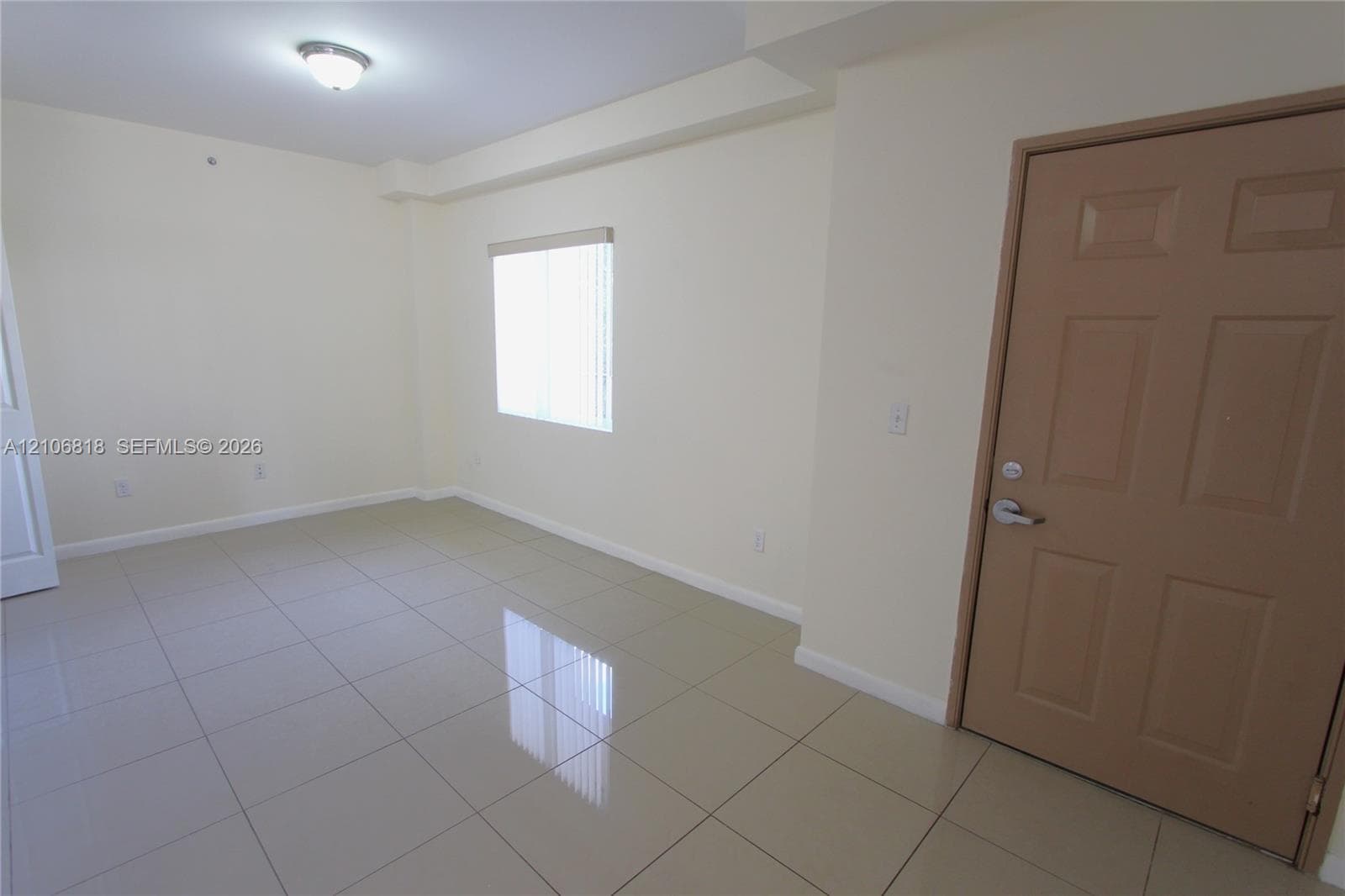 Neutral-toned ceramic tile flooring, solid-core interior door, and a flush-mount ceiling light fixture
