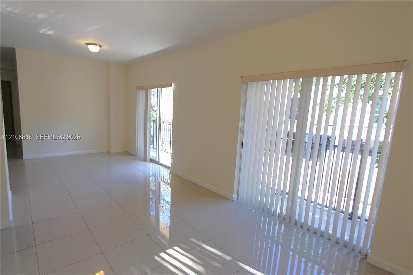 Large ceramic tile flooring, neutral wall tones, and dual sliding glass doors with vertical blinds