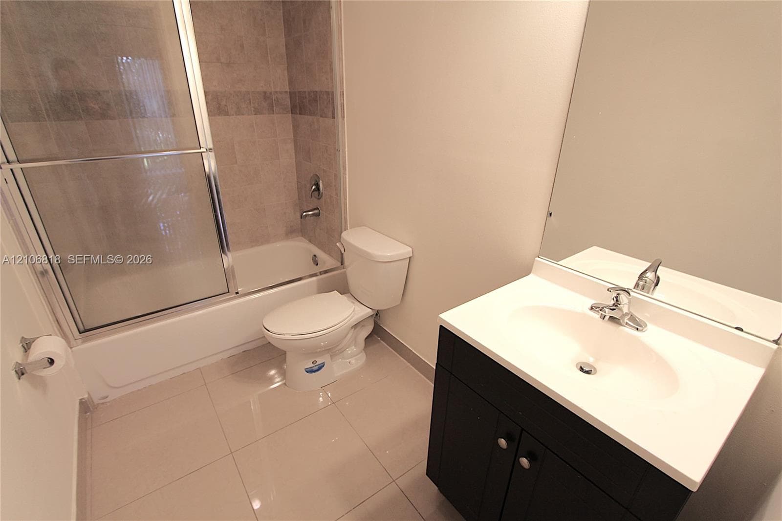 Bathroom featuring a vanity with a white countertop and dark cabinetry, large wall mirror, and a tub-shower combination with sliding glass doors and tiled surround