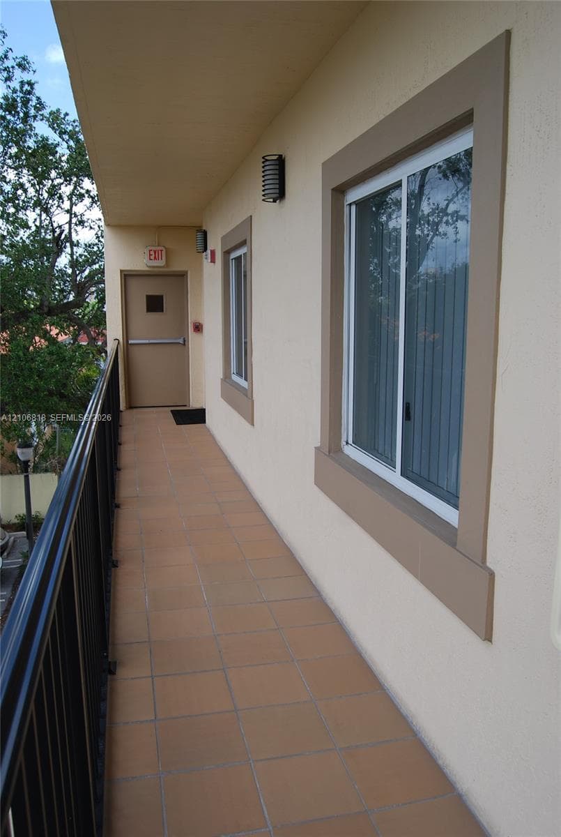 Covered exterior walkway featuring tile flooring, a black metal railing, and wall-mounted sconce lighting