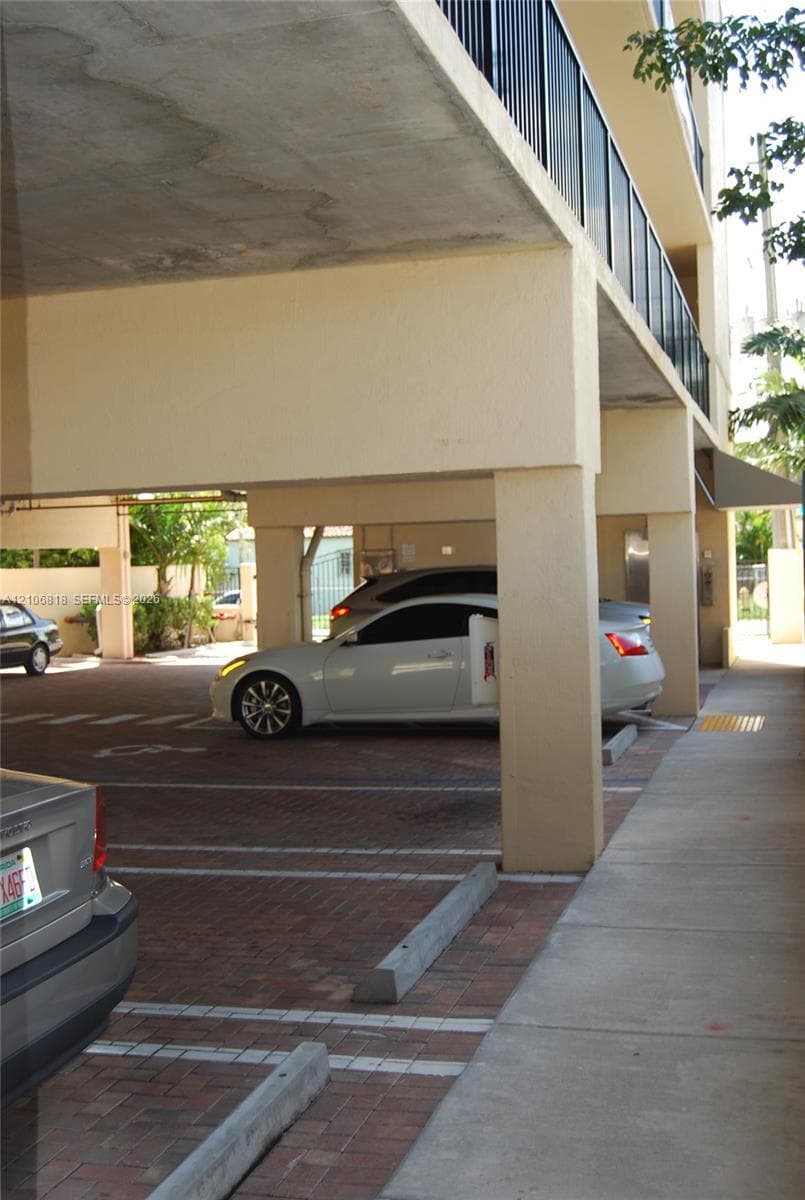 Covered ground-level parking featuring a brick paver surface, concrete support pillars, and a concrete sidewalk