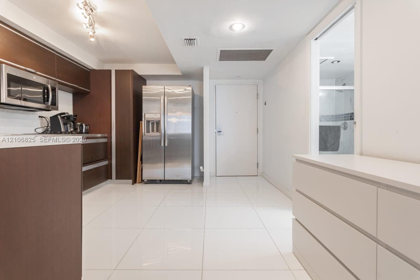 Kitchen featuring dark-toned flat-panel cabinetry, stainless steel appliances, and large-format white tile flooring