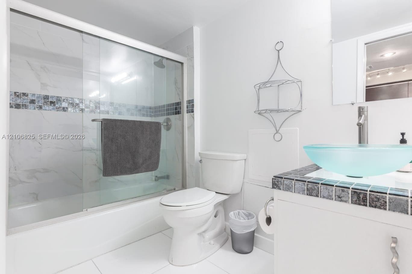 Bathroom featuring a vanity with a tiled countertop, a glass vessel sink, a shower-tub combination with sliding glass doors, and decorative tile accents