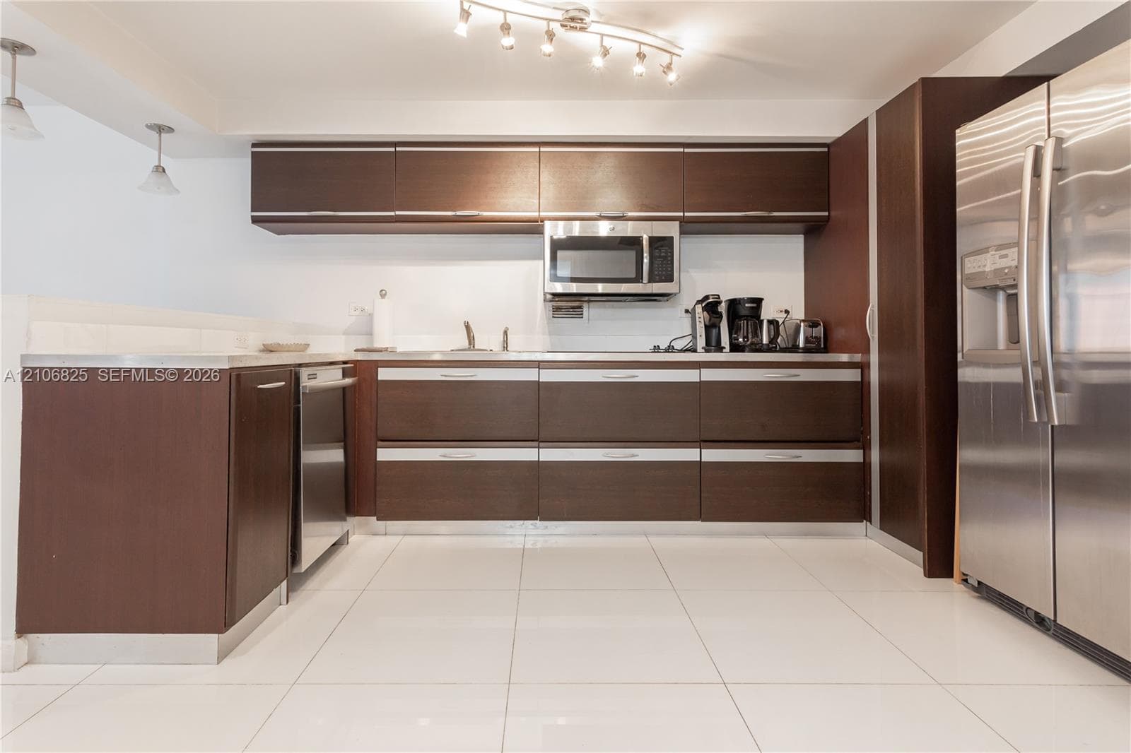 Kitchen featuring dark wood-finish cabinetry, stainless steel appliances, large-format tile flooring, and integrated track lighting