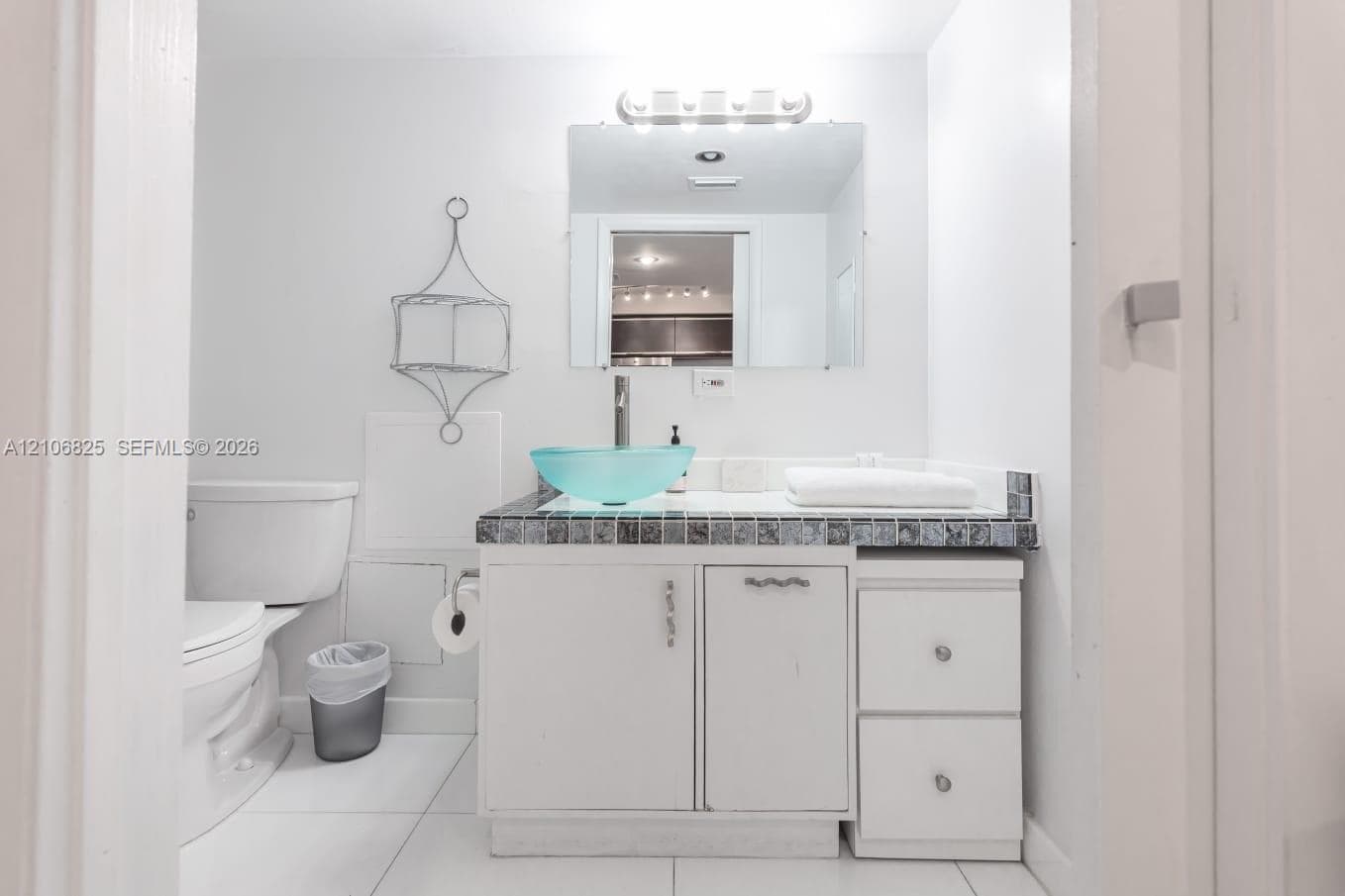 Bathroom featuring a white vanity with built-in cabinetry, tiled countertop, glass vessel sink, and wall-mounted vanity lighting