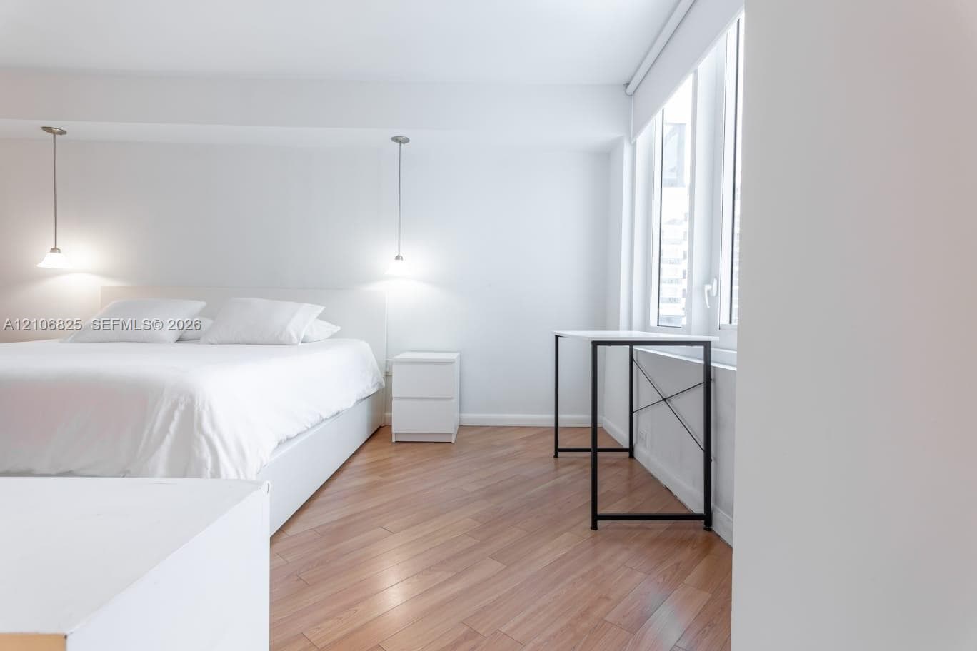 Room featuring wood-finish flooring, dual suspended pendant light fixtures, and expansive window wall with integrated shade