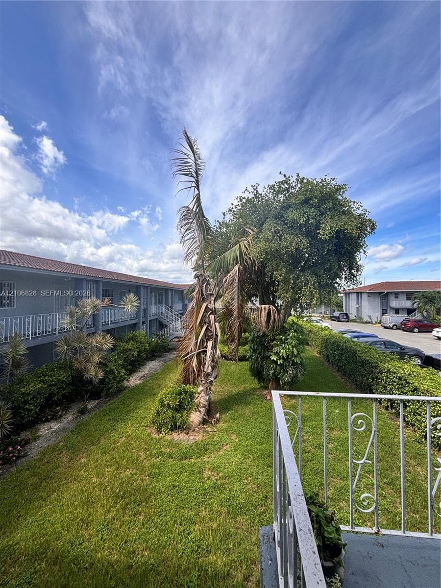 Ground-level exterior featuring manicured lawn, established landscaping, mature palm trees, and metal ornamental railing