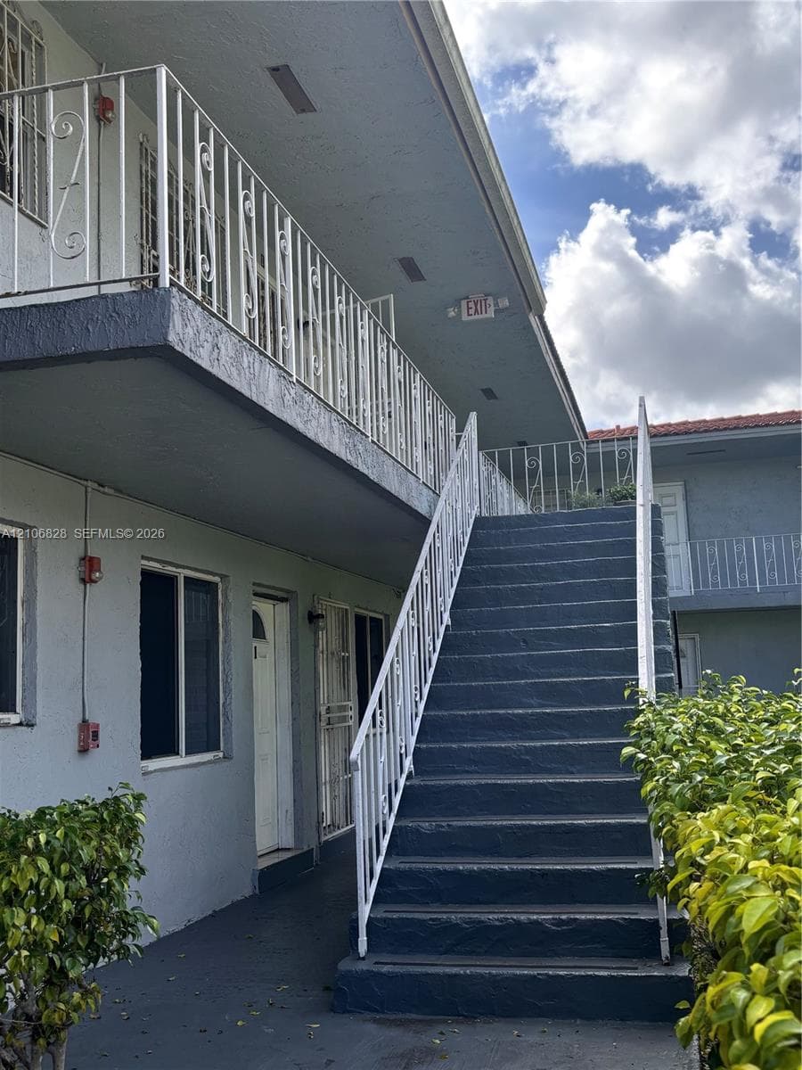 Exterior staircase with metal railings, second-level balcony, and stucco building facade