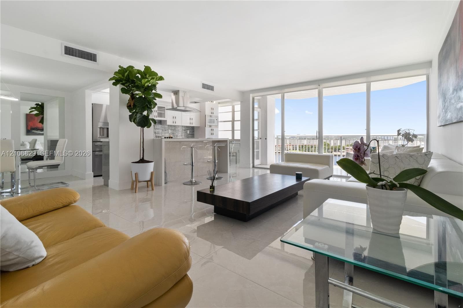 Open-concept interior featuring large-format tile flooring, floor-to-ceiling glass windows, a kitchen island with stone-finish surfaces, stainless steel appliances, and a stainless steel wall-mounted range hood