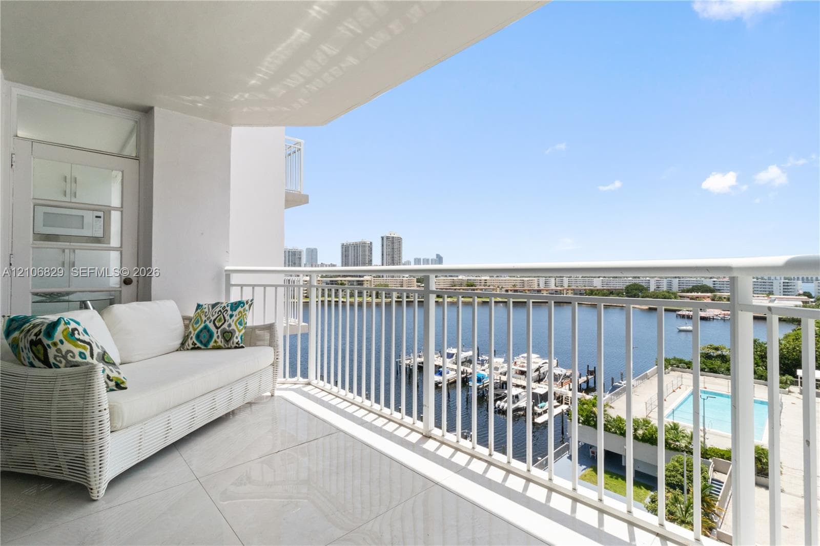 Covered balcony featuring large-format tile flooring and a white metal railing overlooking a marina and waterway