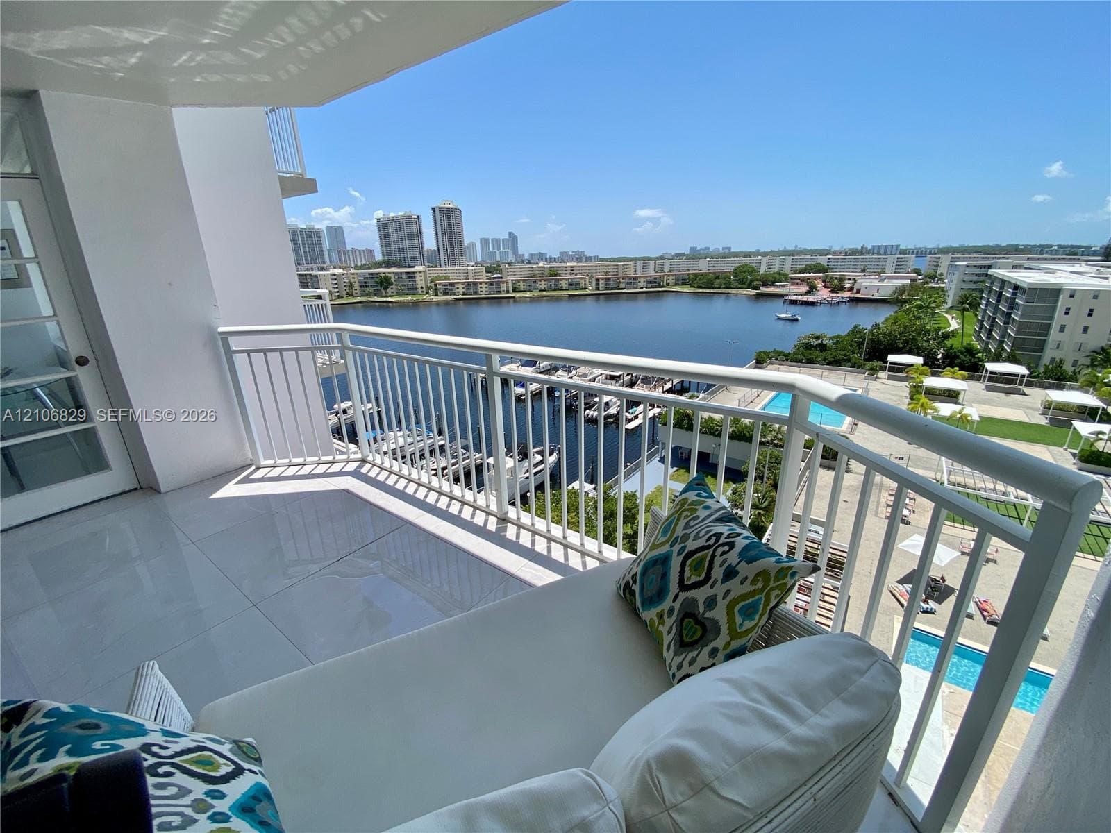 Covered balcony featuring large-format porcelain tile flooring and white metal railing, showcasing direct water and marina scenery