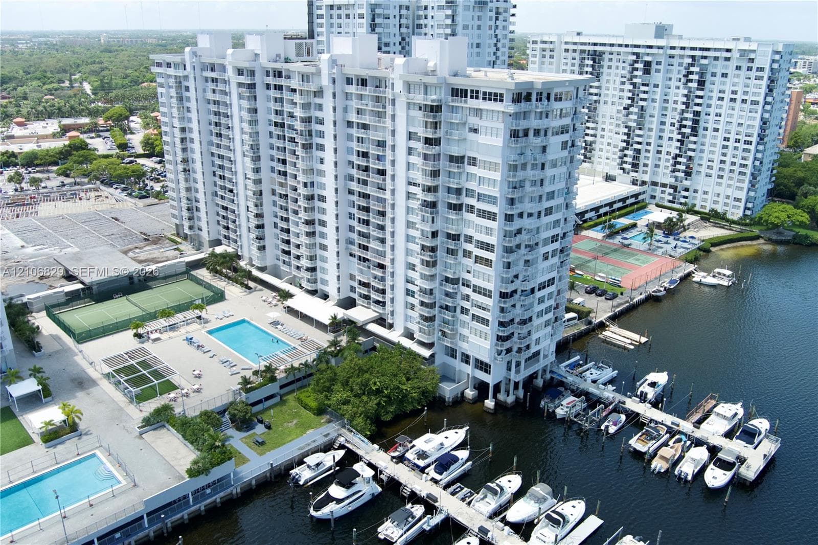 High-rise residential building featuring an on-site marina with boat slips, multiple outdoor swimming pools, and tennis courts situated on a waterfront property