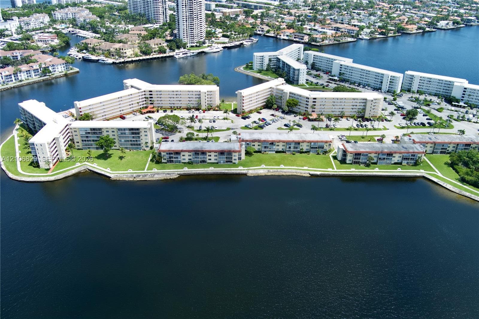 Waterfront residential complex featuring expansive canal frontage, multi-story buildings, paved parking areas, and manicured green space