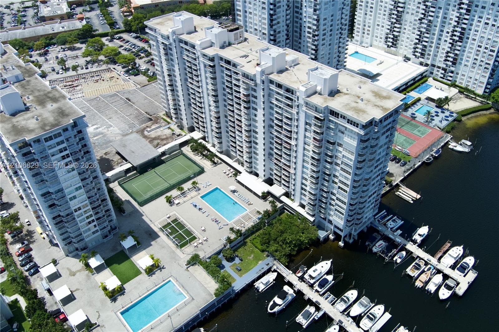 Aerial perspective of a high-rise condominium complex featuring a private deep-water marina, multiple swimming pools, tennis courts, and landscaped grounds