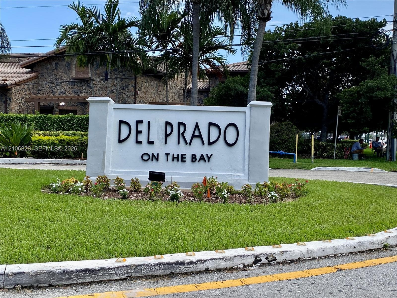 Community entrance signage featuring raised dimensional lettering, surrounded by manicured landscaping, mature palms, and structured masonry columns