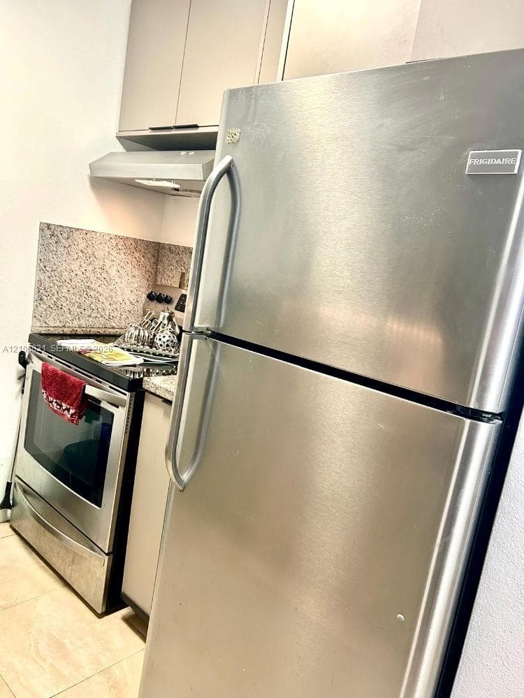 Stainless steel refrigerator and range, stone-composite backsplash, and neutral-toned cabinetry
