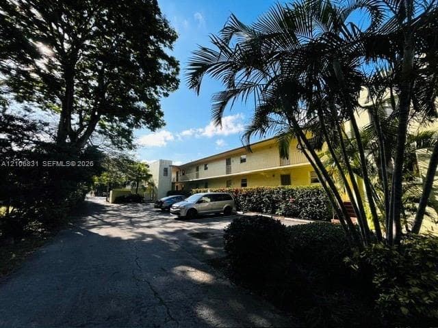 Multi-story exterior featuring paved off-street parking, mature landscaping, palm trees, and established perimeter shrubbery