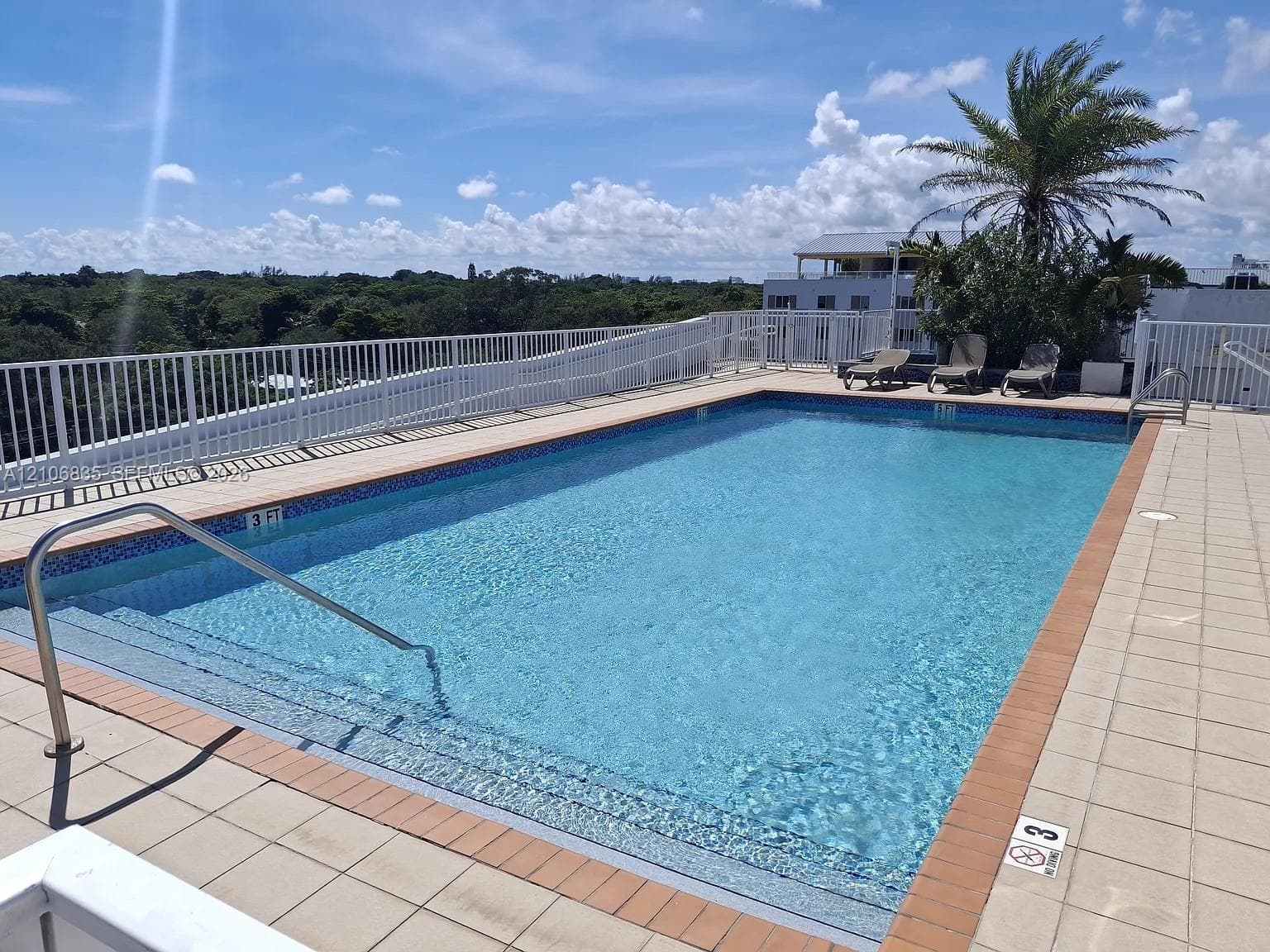 Rooftop swimming pool featuring tiled decking, metal perimeter fencing, integrated ladder, and tile coping