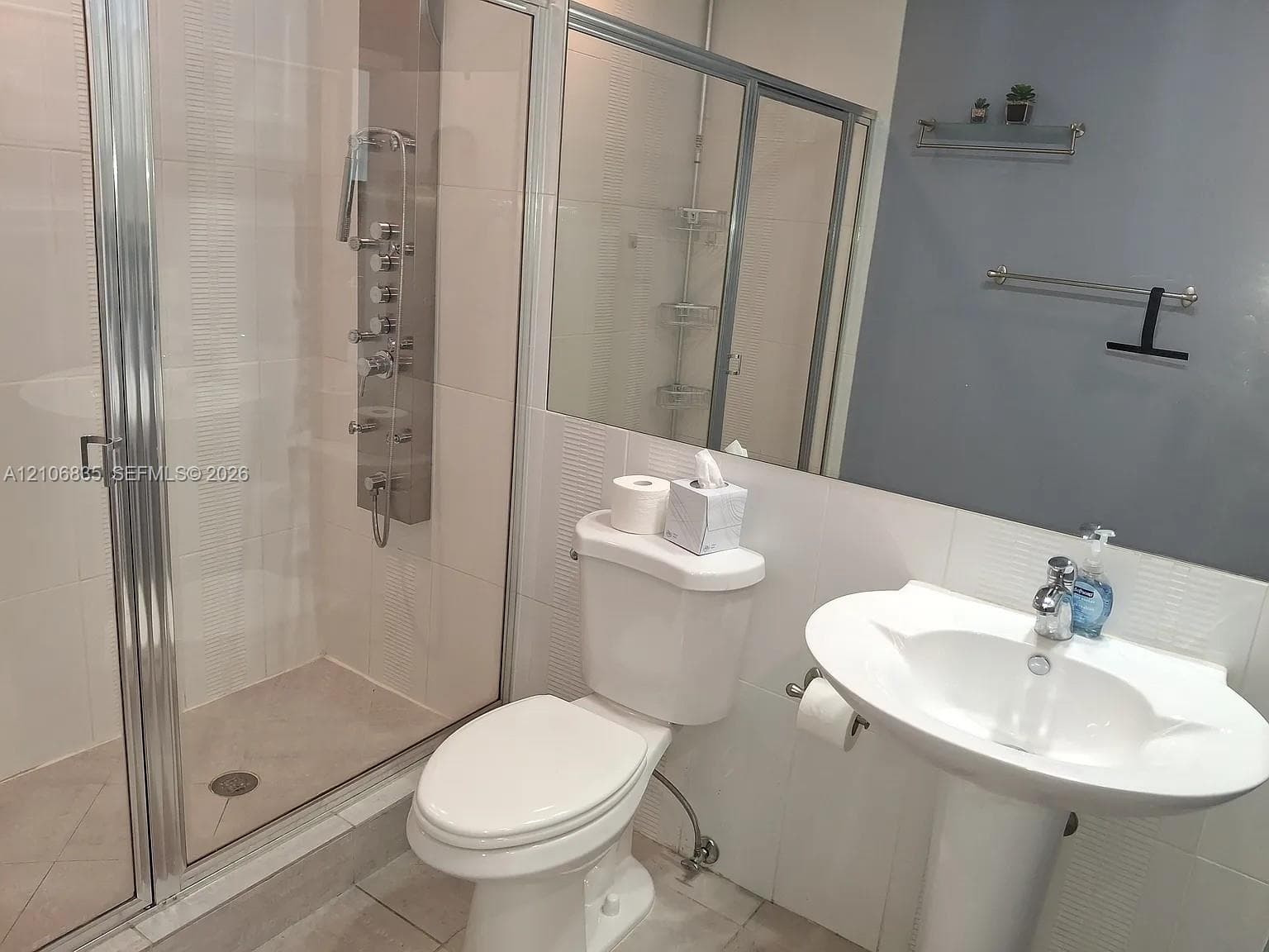 Walk-in shower enclosure featuring a multi-jet shower panel, pedestal sink, chrome-finished hardware, and large-format wall tiling