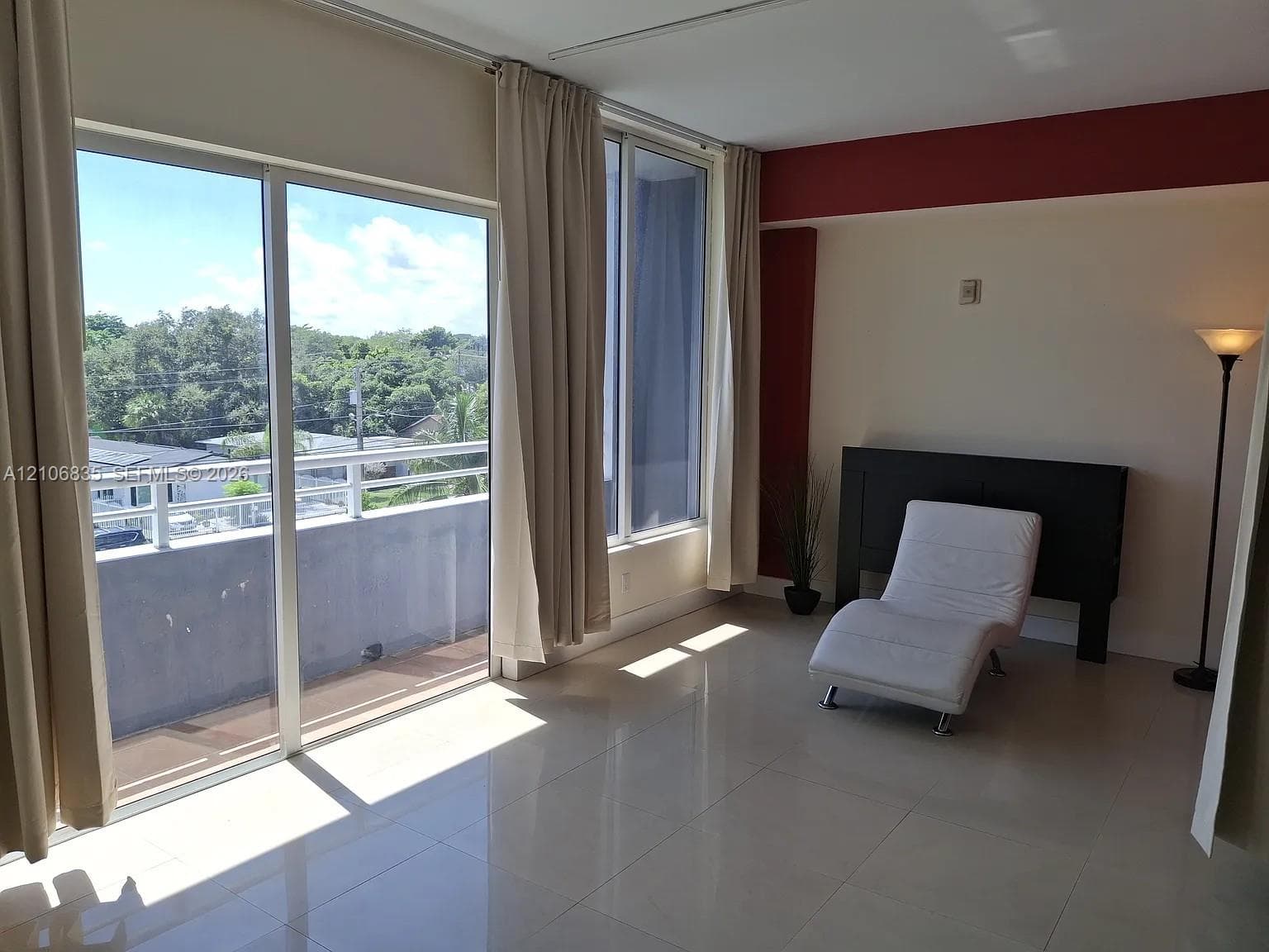 Floor-to-ceiling sliding glass doors, private balcony with metal railing, high-gloss tile flooring, and neutral wall tones with decorative accent trim