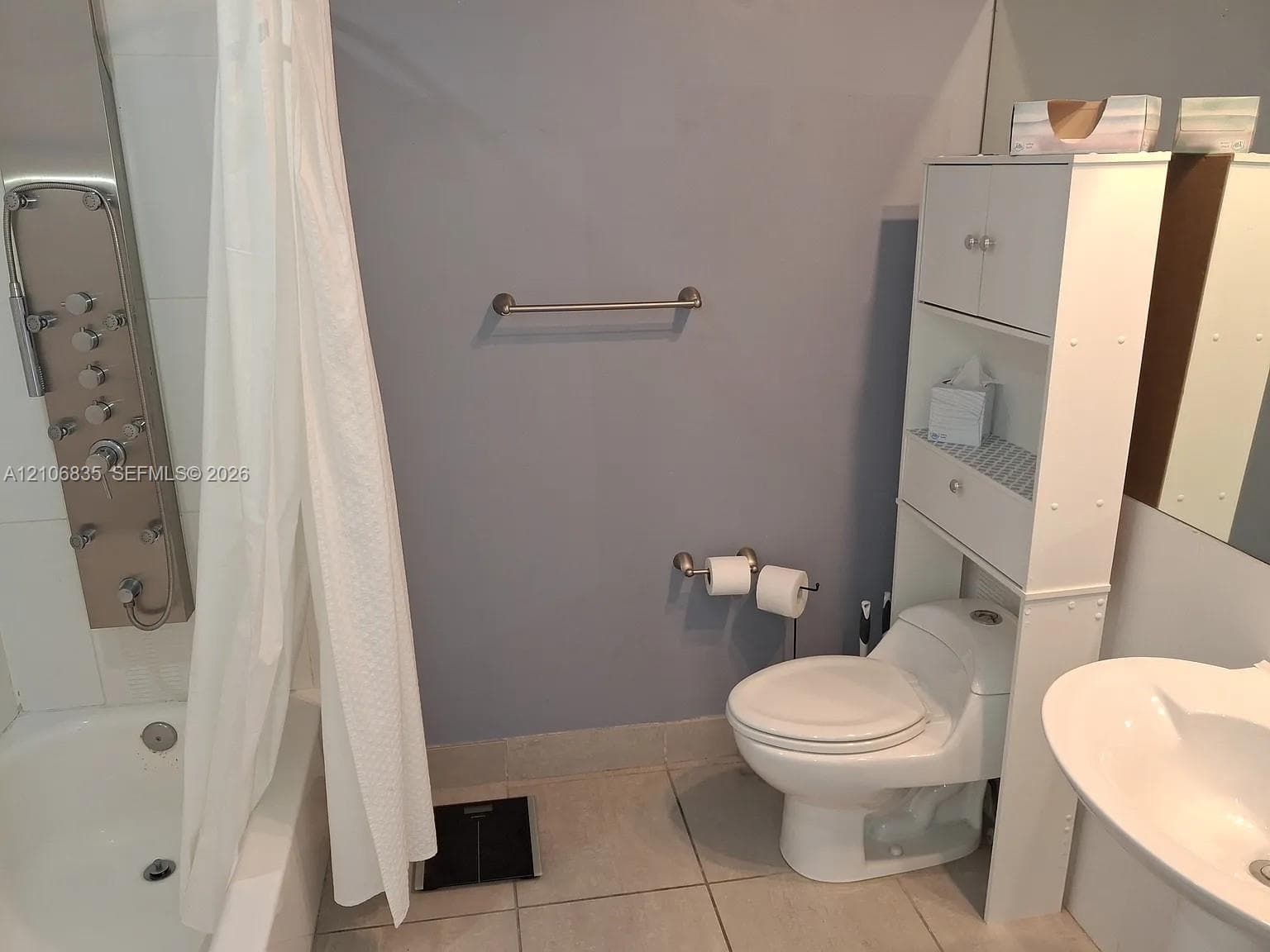 Bathroom featuring a stainless steel shower panel with multi-function spray heads, a white porcelain tub, tile flooring, and brushed nickel hardware