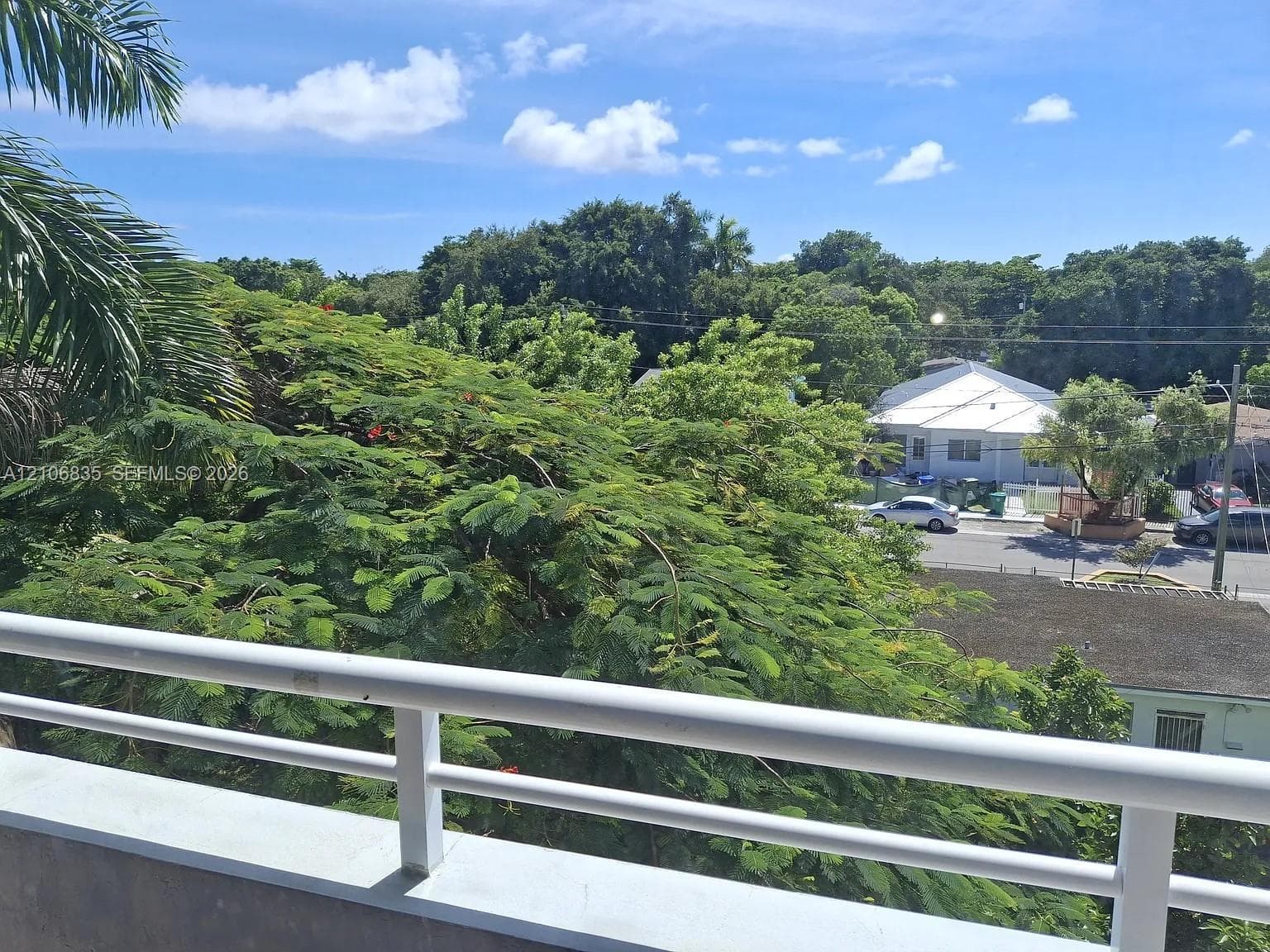 Elevated balcony featuring a white metal railing and greenery-rich surroundings