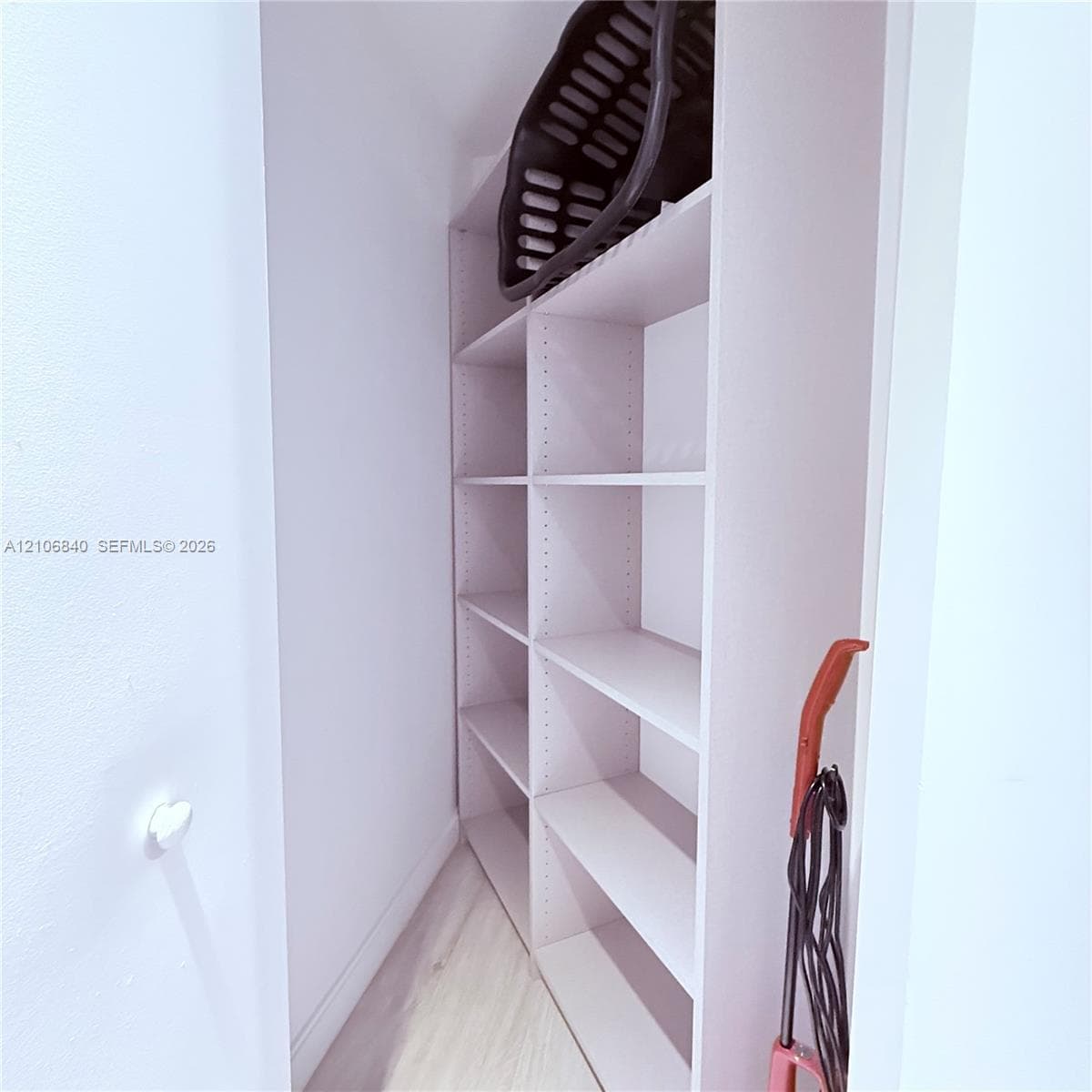 Built-in, floor-to-ceiling white shelving with adjustable cabinetry and light-toned wood-finish flooring