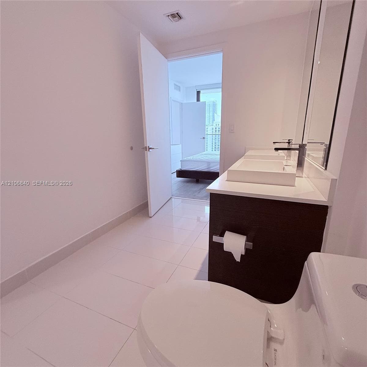 Bathroom featuring a dark wood-finish vanity with dual rectangular vessel sinks, light-toned stone countertop, polished tile flooring, and large-format wall mirror