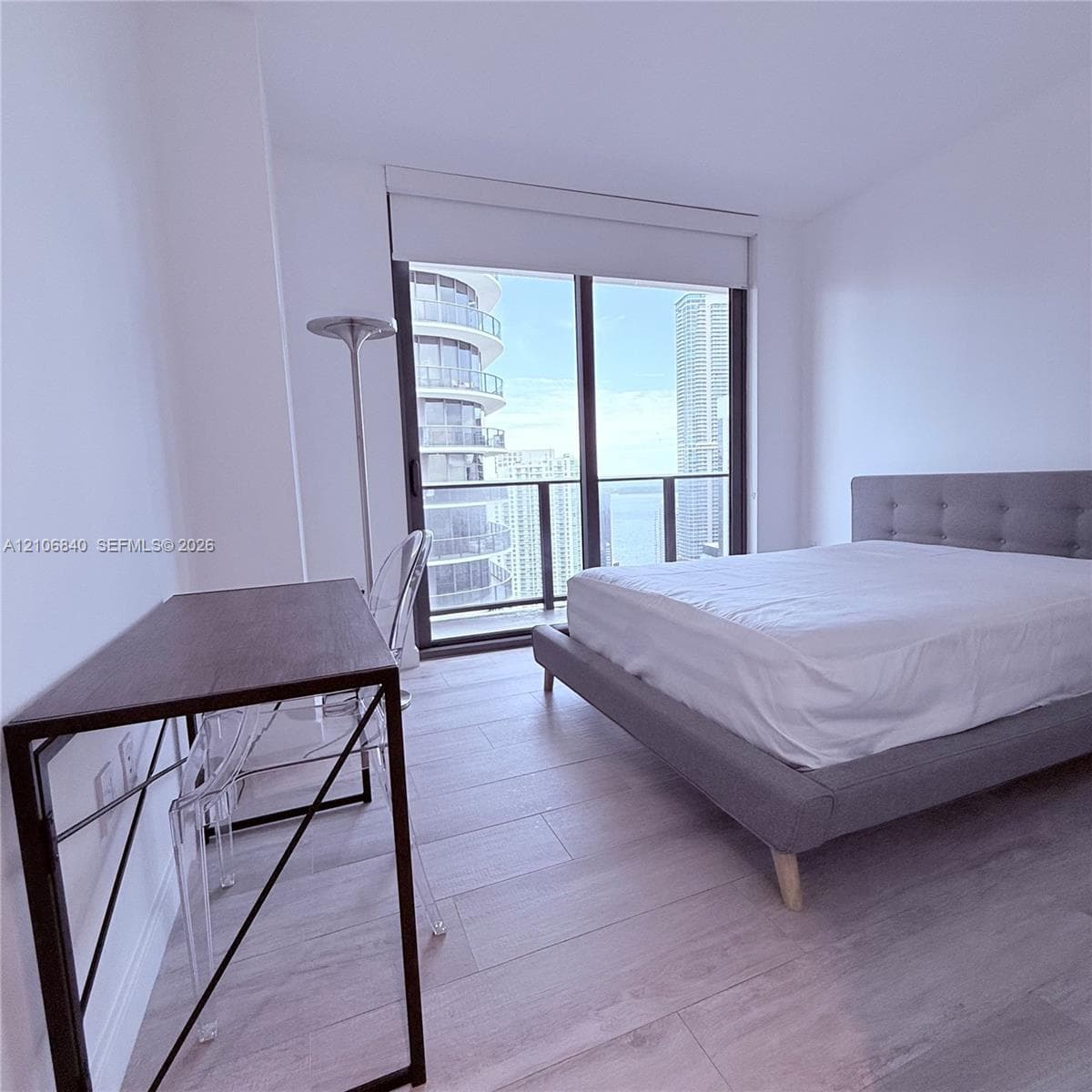 Floor-to-ceiling windows with roller shades, wood-finish flooring, and a private balcony featuring a glass-panel railing