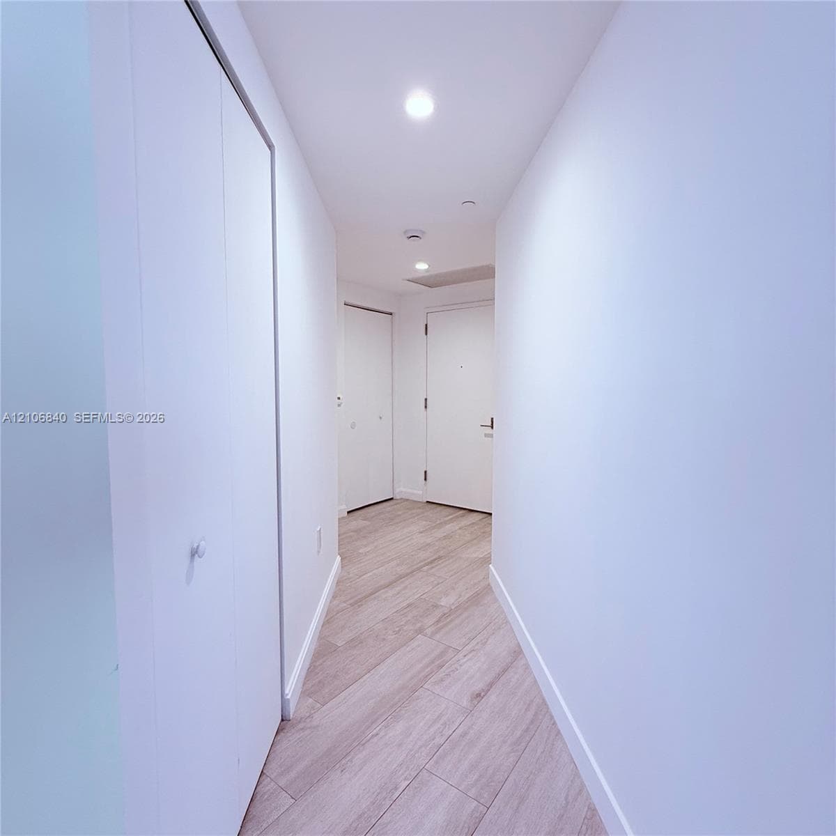 Hallway featuring wood-finish flooring, recessed lighting, and multiple interior closet doors with white hardware